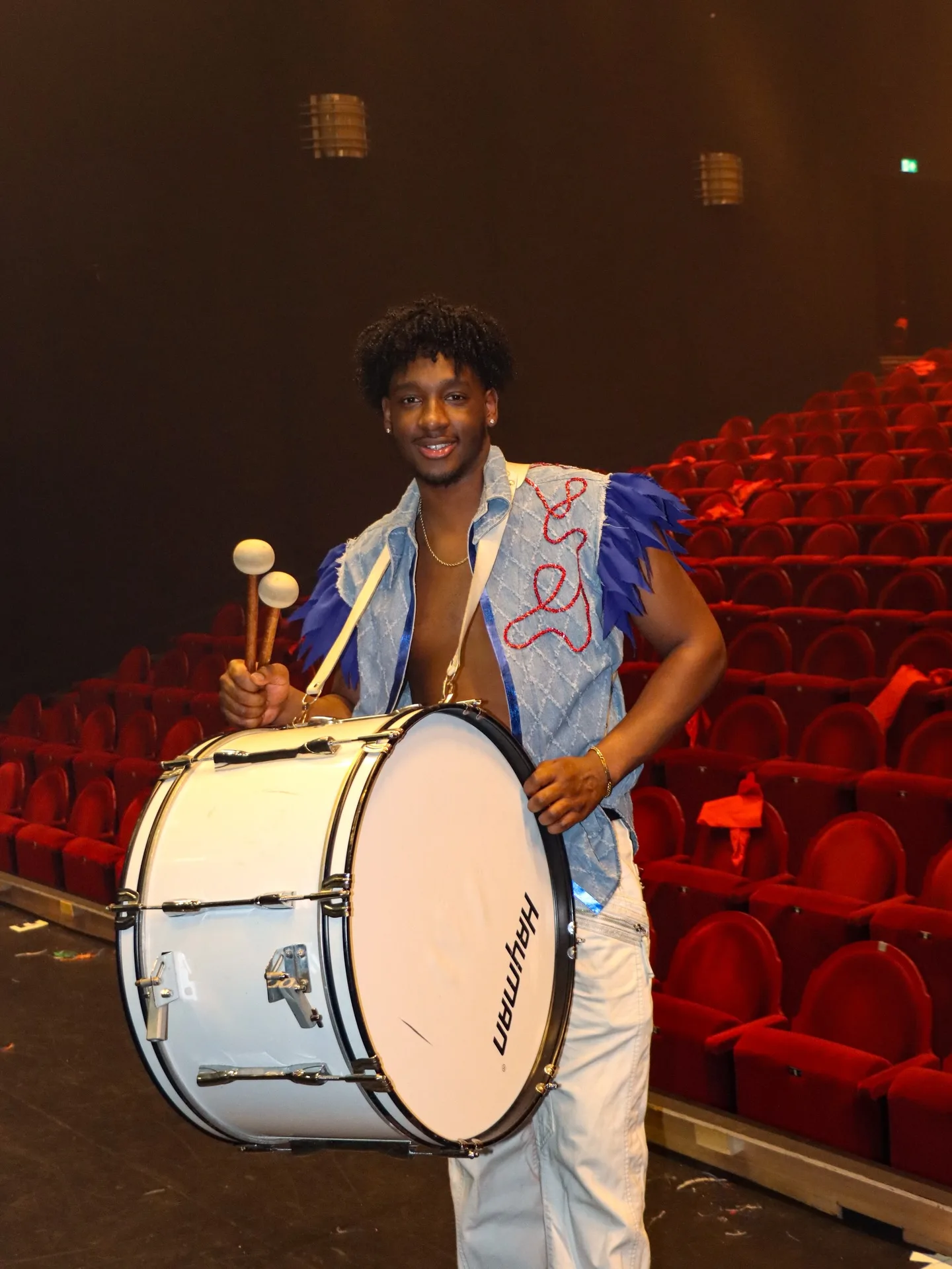 Drummer met een witte basdrum in een theaterzaal met rode stoelen