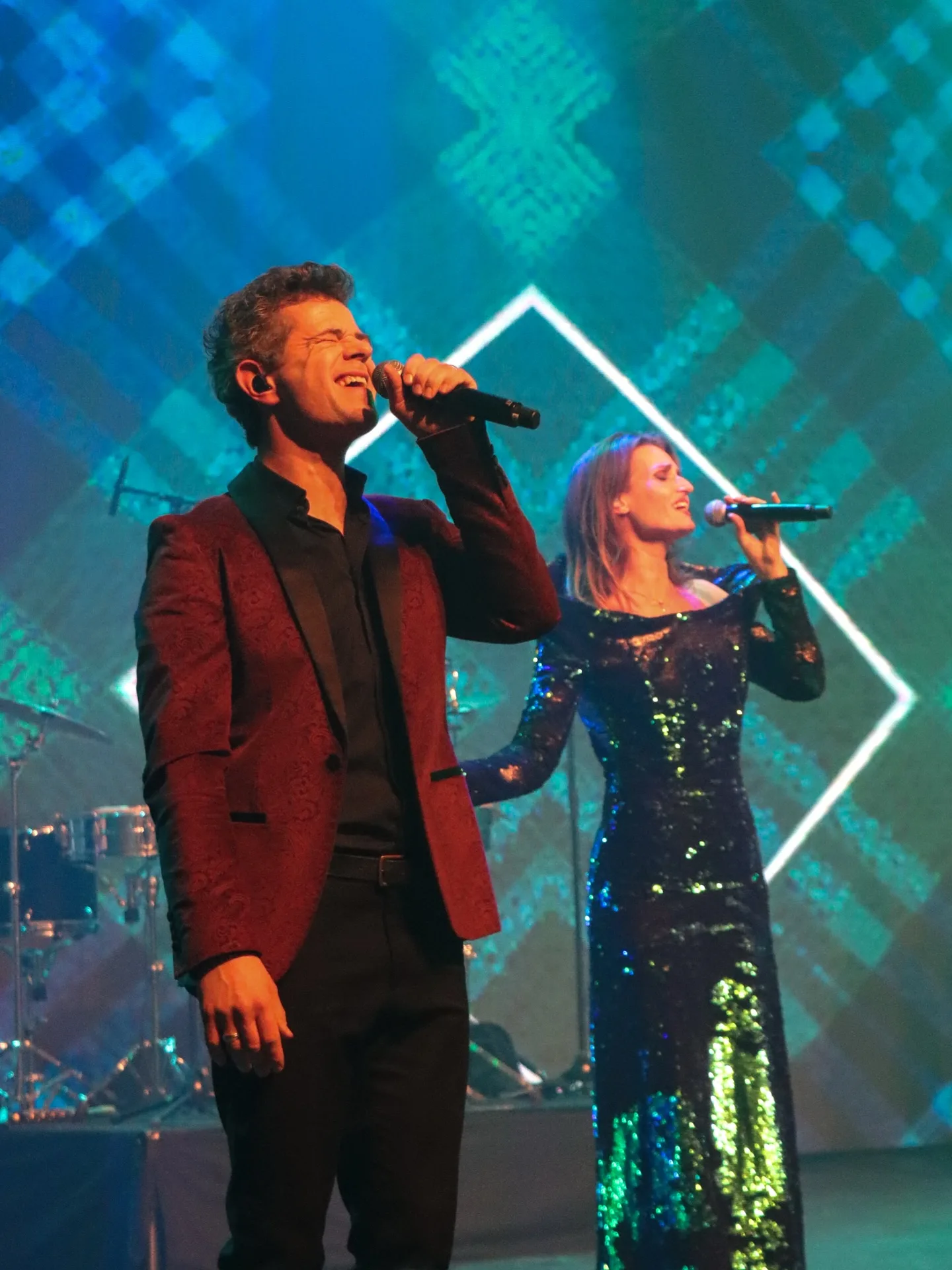 Zanger en zangeres zingen samen op het podium in blauw licht
