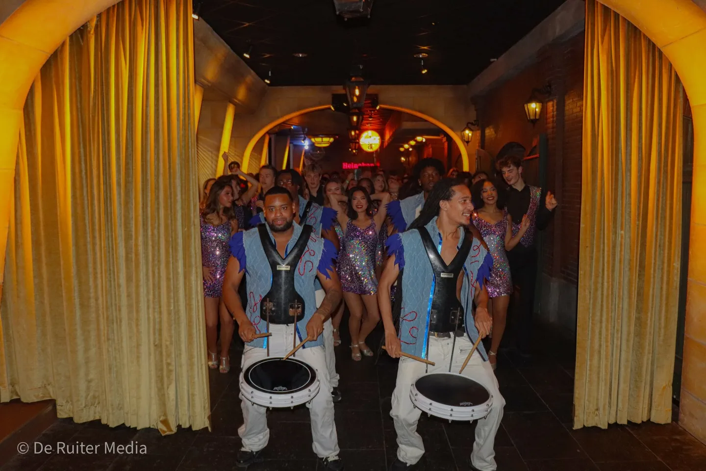 De drumband van Fire & Rhythm International in blauw-witte kostuums tussen het publiek