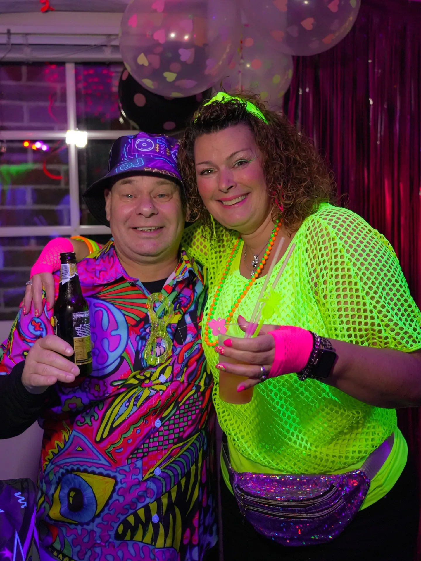 Twee vrouwen in neon outfits lachen in de camera op een 50e verjaardag